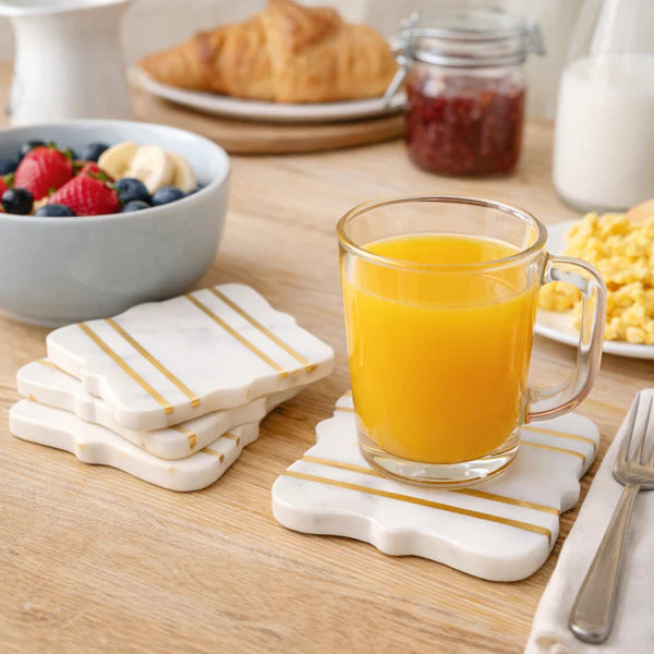 Bracket Luxe Marble Coasters with gold stripe accents holding glass mug of orange juice on wooden breakfast table