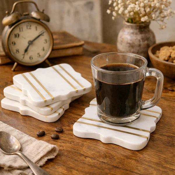 Glass of coffee on a marble coaster with striped design, surrounded by an alarm clock, books, and a vase on a wooden table.