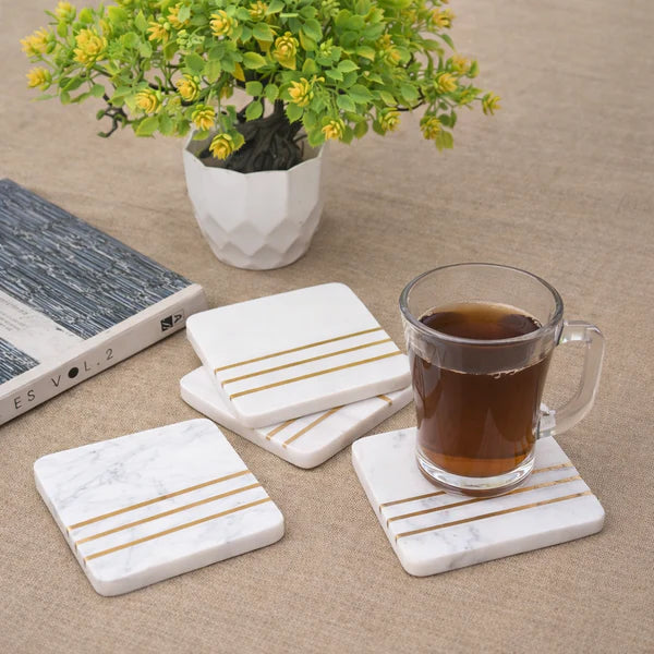 Set of marble coasters with gold stripes on a table with a cup of tea and a plant.