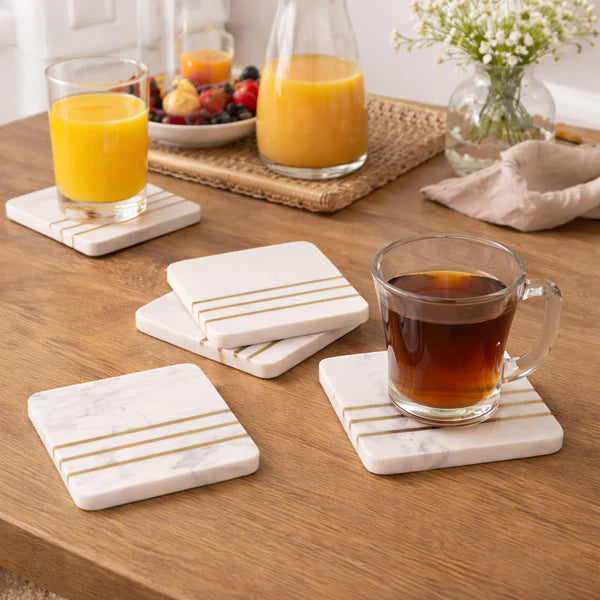 Set of marble coasters with gold stripes on a wooden table with drinks.