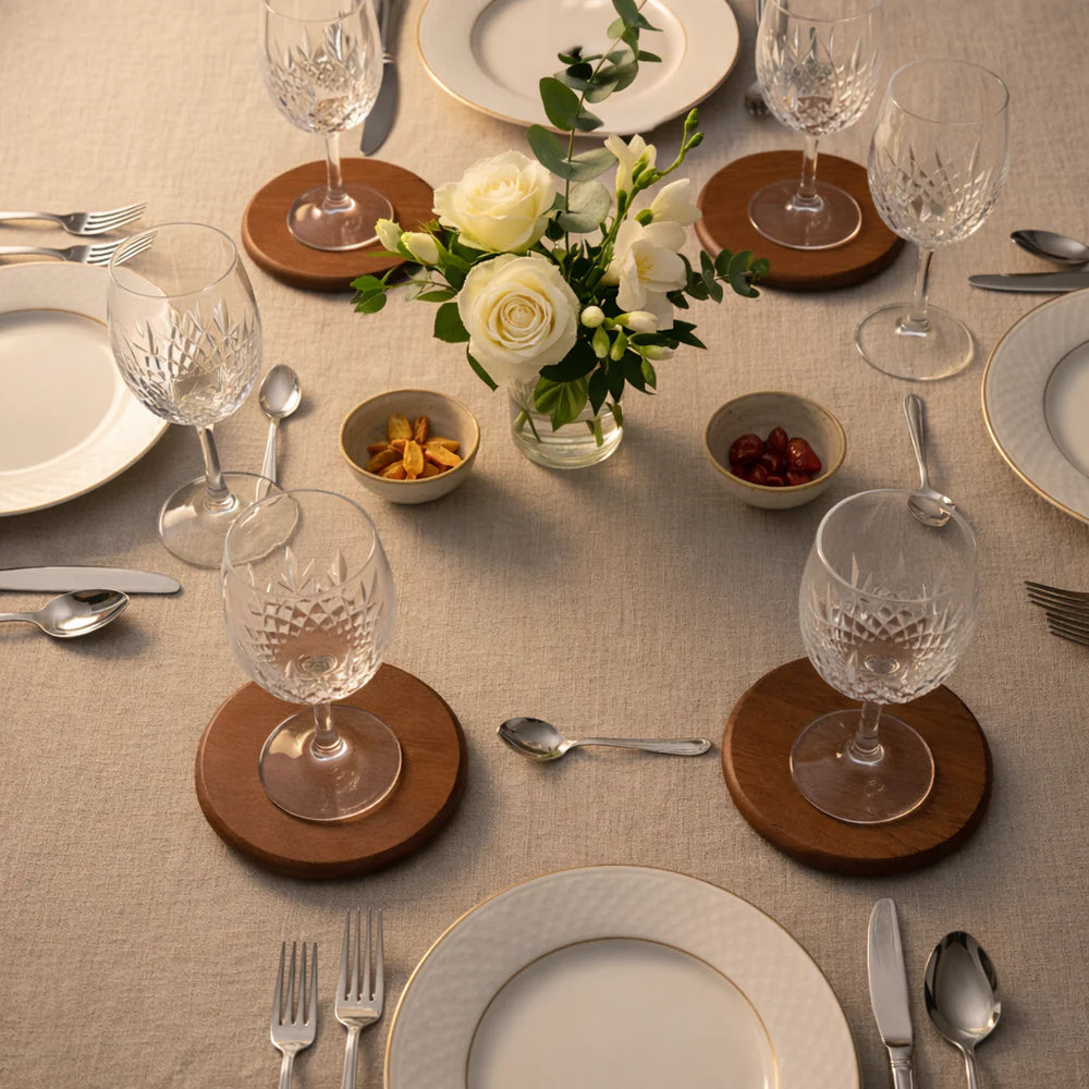 Elegant table setting with glasses, plates, and flowers on a beige tablecloth on Terra Round Wooden Coasters